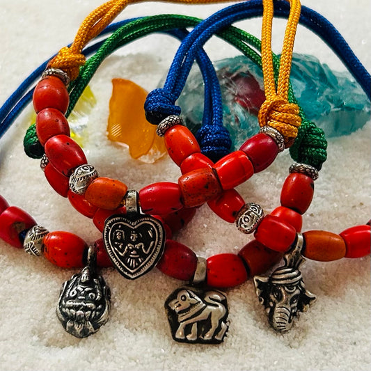 Flat lay of Sacred Sherpa Talisman bracelets with colorful adjustable cords, antique red coral glass beads, and silver spiritual charms